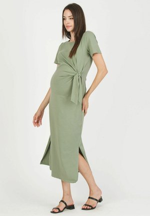Abito premaman verde oliva con maniche corte, dettagli con nodo laterale e spacchi alti fino alla coscia su entrambi i lati; realizzato in tessuto morbido e stretchy.