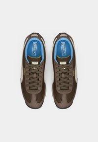 Ein Paar braune Puma Easy Rider Sneaker mit blauen Innensohlen und beigem Puma-Logo an den Seiten, von oben auf einem weißen Hintergrund betrachtet.