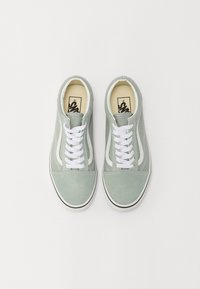Sneaker in suede di colore verde chiaro con lacci bianchi e dettagli laterali. Punta arrotondata e suola in gomma con un bordo nero lungo la base.