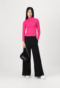 Piele rožā turtleneck džemperis, plata melna bikses un melna rokassoma ar ķēdītes siksnu, ar baltu tekstu. Apģērbu kompletē sporta apavi.