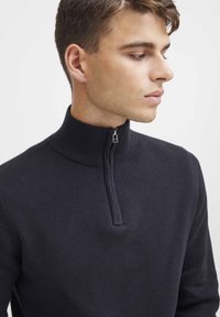 Marineblauer Strickpullover mit hohem Kragen und einem halben Reißverschluss, der über eine gerippte Textur verfügt. Eng anliegendes Design ohne sichtbare Muster oder Akzente.
