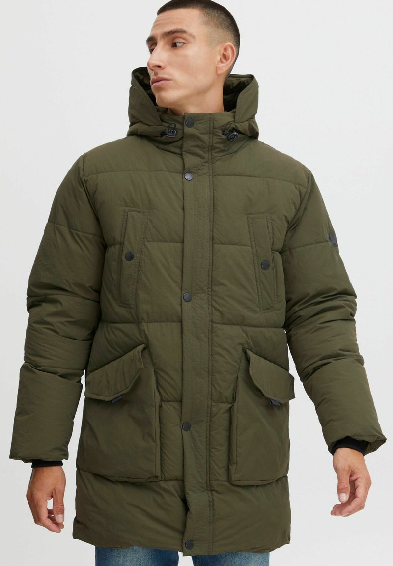 Chaqueta acolchada verde con capucha, que presenta un cierre frontal de botones, dos grandes bolsillos frontales y una textura acolchada. Corte estándar con un diseño casual.