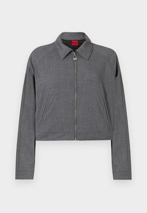 Szara kurtka z długim rękawem z kołnierzem, zapięciem na zamek błyskawiczny z okrągłym uchwytem oraz bocznymi kieszeniami, rozłożona na płasko na białym tle.