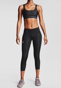 Svart sport-bh och leggings, tillverkade av elastiskt material. Leggings är capri-längd, har hög midja och en subtil logotyp.