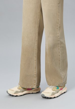 Pair of beige wide-leg pants worn with cream and pastel-colored sneakers on a gray background.