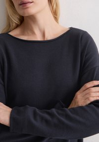 Donkerblauw shirt met lange mouwen, boothals, geribbelde textuur en een losse pasvorm. Licht omgerolde manchetten zonder zichtbare sluiting.