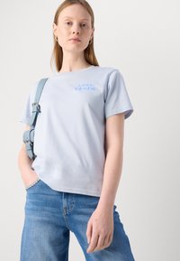 Lyseblå t-skjorte med kort erme, med teksten "LOVE CRUSH" i en litt mørkere blåfarge. Stoffet ser mykt og glat ut.
