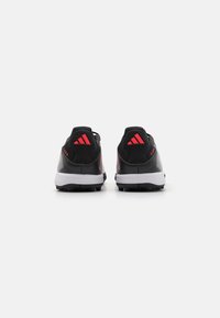 Zapatillas deportivas negras con detalles rojos, que presentan una parte superior sintética, un diseño texturizado, un acolchado en el collar y una suela blanca con tacos para mayor agarre.