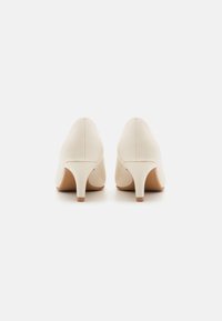 Chaussures à talons hauts beiges avec un bout pointu, une texture cuir lisse et un talon fin. Les semelles sont marron avec un minimum de détails.