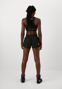 Soutieno desportivo preto com alças ajustáveis, combinado com calções elásticos pretos com bolsos e um logo. Meias azuis com detalhes vermelhos.
