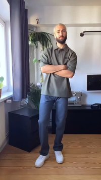 Άνδρας με ανοιχτόχρωμα μαλλιά και γένια στέκεται με τα χέρια σταυρωμένα σε ένα δωμάτιο με φυτά, μια ραπτομηχανή και ξύλινο πάτωμα.