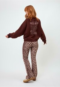 Felpa oversize marrone con testo grafico sulla schiena abbinata a leggings flare leopardati beige e marroni, completato con scarpe platform color beige.