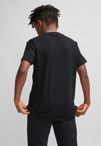 Camiseta de algodón negra con mangas cortas, cuello redondo y corte relajado, mostrada desde la parte de atrás. Diseño minimalista sin logotipos visibles.