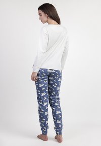 Top blanco de manga larga combinado con pantalones azules de estampado que presentan osos polares y copos de nieve, fabricados con tela suave y con un diseño ajustado.