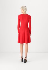 Rdeča obleka z dolgimi rokavi, ki ima oprijet bodice in razširjen krilo. Narejena iz gladkega materiala, z okroglo izrezom in nabranimi detajli na ramenih.