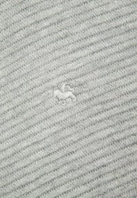 Jasnoszara tkanina o ryflowanej fakturze. Zawiera małe, haftowane logo stylizowanego zwierzęcia w kolorze białym, subtelnie umieszczone w splocie.