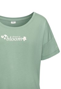 Žalia trumpomis rankovėmis marškinėliai su apvalia iškirpte ir balto teksto užrašu „choose to bloom“ krūtinės srityje, šalia kurio yra mažos gėlės grafikos.