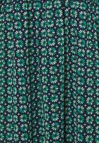 Kukallinen kangas, jossa vihreitä ja valkoisia kukkia tumman laivastonsinisen taustan päällä, toistuvia, symmetrisiä kuvioita ja pehmeä pinta.