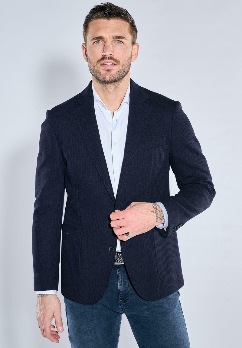 Navy pinstriped blazer with two front pockets, single button closure, notched lapels. Styled over a light blue shirt and denim jeans.