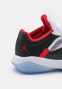 Zapatilla negra con acentos rojos y malla blanca, con un upper de cuero texturizado, cuello acolchado y suela translúcida con un detalle de logo.