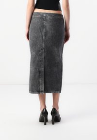 Svart denim midi skjørt med vertikale striper, tettsittende liv, og splitt bak. Matchet med svarte høye hæler.