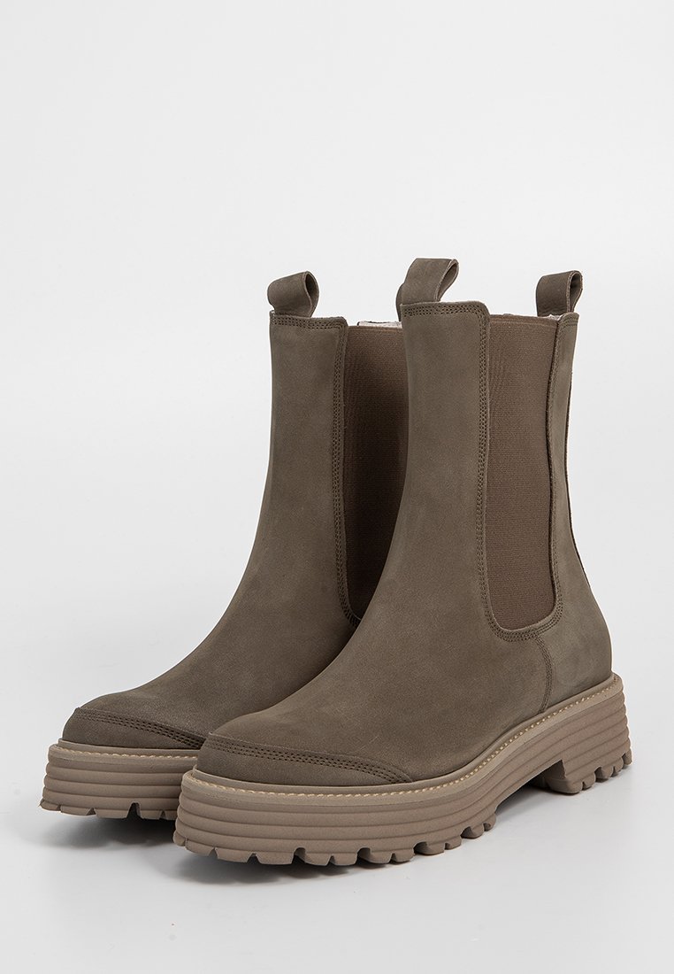 Ein Paar braune Wildleder Chelsea-Stiefel mit robusten Gummisohlen und elastischen Seiteneinsätzen, Ziehschlaufen vorne und hinten, auf einem schlichten hellen Hintergrund.