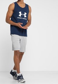 Laivastonsininen tankkitoppi, jossa valkoinen "Under Armour" -logo, yhdistetty harmaisiin urheilushortseihin. Päällä navy-siniset urheilukengät, joissa valkoiset yksityiskohdat.