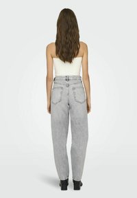 Pantalones vaqueros de mezclilla gris de tiro alto con un corte relajado, que cuentan con dos bolsillos traseros y un detalle de costura visible. Llevados con una blusa blanca ajustada.