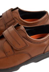 Scarpe di pelle marrone con chiusure in Velcro, forma arrotondata, suole in gomma e fodera interna arancione, con dettagli di cucitura a contrasto.