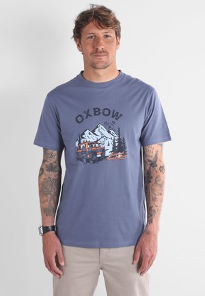 T-shirt à manches courtes et col rond en coton bleu doux, avec un motif graphique de montagnes et d'un camion ; présente le texte "OXBOW" et "Beyond Boundaries".