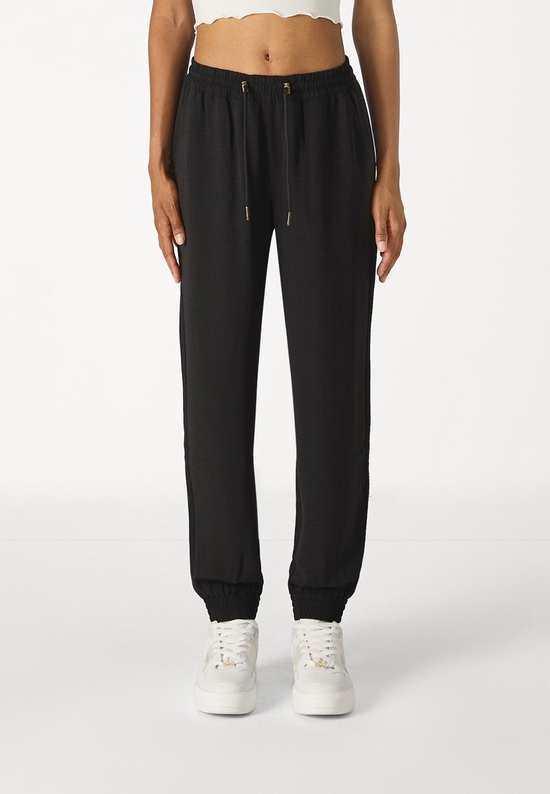 Black jogger pants with elastic cuffs and drawstring waist. Made from lightweight fabric, featuring subtle texture and gold-tone hardware accents.