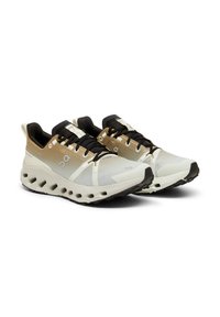 Scarpe da corsa con un upper beige e bianco, dotate di materiale in mesh, accenti neri e una suola distintiva imbottita con aperture.