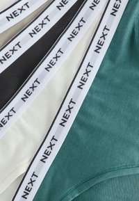 Quatre paires de sous-vêtements en vert, crème, noir et beige avec des bandes élastiques blanches étiquetées "NEXT" en texte noir.
