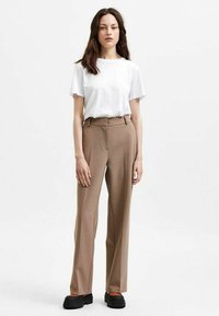 Beige op maat gemaakte broek met een hoge taille, rechte pijpen en zijzakken, gecombineerd met een plain wit T-shirt en stevige zwarte schoenen.