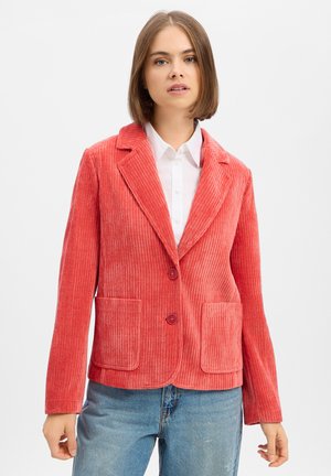 Woman wearing a coral pink corduroy blazer over a white button-up shirt and light blue jeans against a white background.
