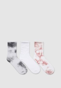 Trzy pary skarpetek: po lewej w czarno-szarej tie-dye, w środku gładkie białe, po prawej w biel z różowym wzorem tie-dye. Materiał mieszanka bawełny.
