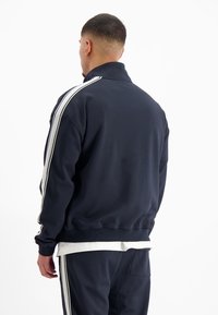 Marineblauwe sweatshirt met hoge kraag, witte zijkanten, geribbelde manchetten en een losse pasvorm, van achteren gezien.