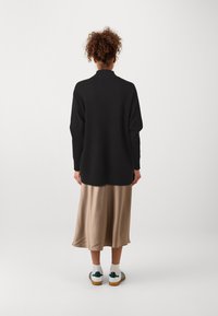 Svart stickad tröja med hög hals, oversized passform och ribbad fåll, kombinerad med en beige satängkjol och vita sneakers med gröna detaljer.