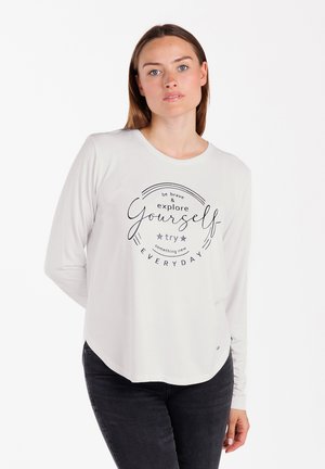 Chemise à manches longues, grise claire, avec un col rond et un message imprimé : "sois courageux et explore-toi, essaie quelque chose de nouveau TOUS LES JOURS."