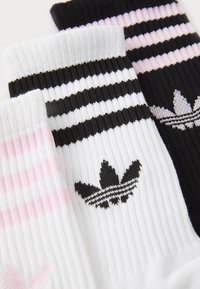 Trīs pāri sporta zeķu: baltas ar melnām svītrām, melnas ar rozā svītrām, un pilnīgi melnas. Iespējas ribota tekstūra un logotipa akcenti.