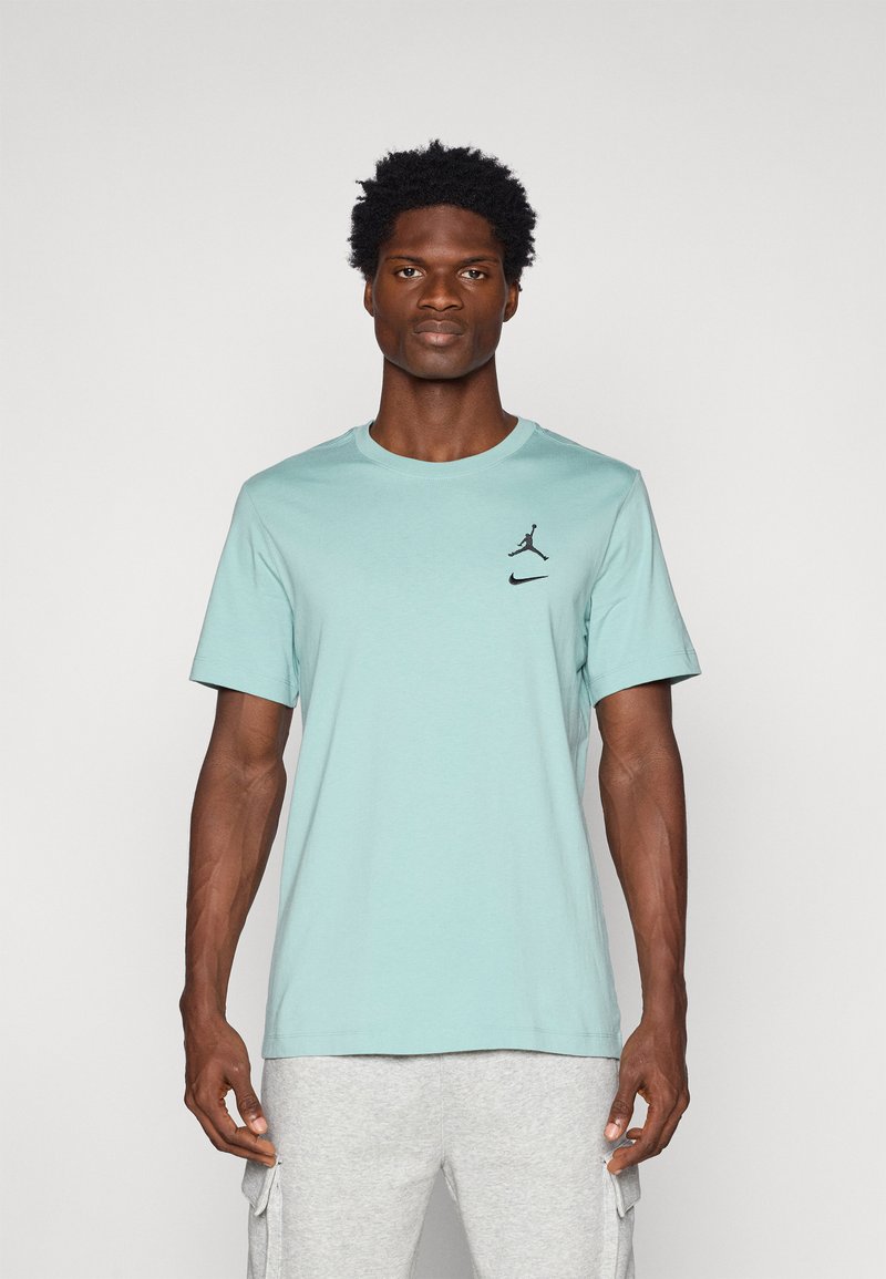 Camiseta corta de manga en un tono azul turquesa claro con pequeños logotipos negros de Nike y Jordan en el pecho. Tejido suave y diseño clásico de cuello redondo.