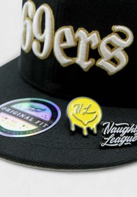 Musta lippu, jossa on valkoisella ja kullalla kirjailtu "69ers" -teksti, hologrammitunnus ja kaksi nappia: keltainen hymyilevä naamari ja musta "Naughty League" -logo.