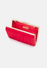 Pochette en satin rouge avec quincaillerie dorée, design plissé et fermeture à pression. Intérieur doublé, comportant une étiquette de marque.