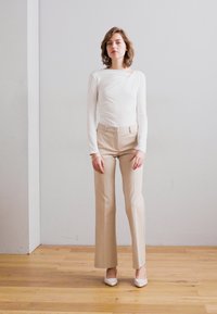 Bodysuit blanco de manga larga con escote drapeado, combinado con pantalones beiges de corte entallado y tacones blancos. Texturas de tela simples y suaves.