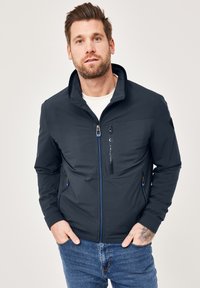 Navy blue softshell jacket with stand collar, zippered pockets, and contrasting blue accents. Fabric appears smooth and water-resistant.