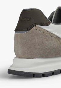 Zapatillas de ante y textil en gris y beige con un contrafuerte en marrón oscuro, que presentan una franja lateral blanca en forma de onda y una suela de goma texturizada.