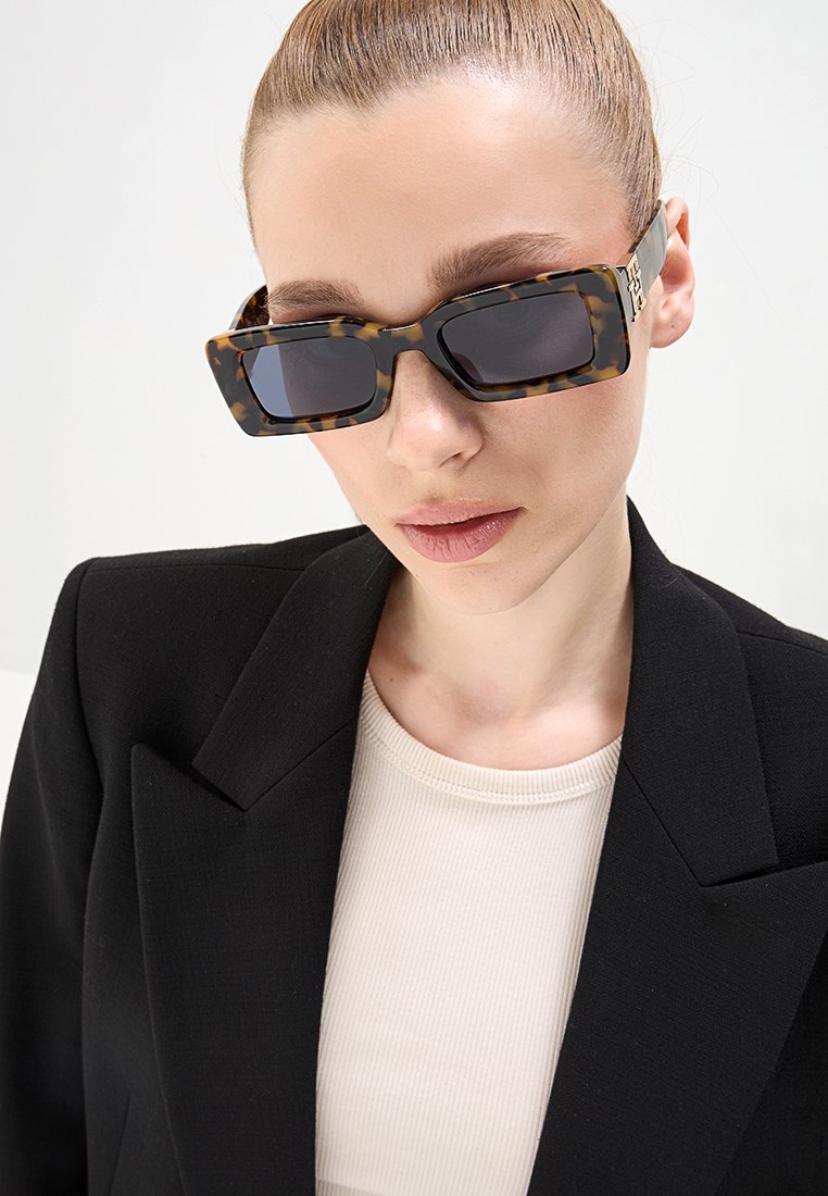 Lunettes de soleil rectangulaires en écaille de tortue avec des verres foncés, présentant un design géométrique audacieux et des attaches sur les branches en métal doré.
