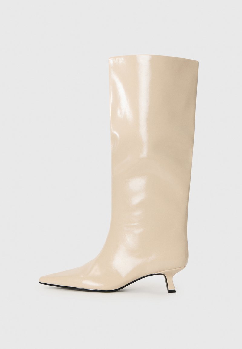 Beige patent leather knee-high boot with a pointed toe, minimalistic design, and a small, block heel. Smooth texture and glossy finish.