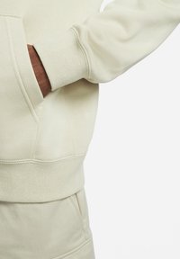 Ljuskrämfärgad sweatshirt med texturerad yta, försedd med kängurufickor och ribbstickade ärmmuddar. Inga synliga logotyper eller ytterligare mönster.