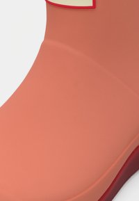 Korale gumijasti škornji za dež, z mat zaključkom, zaobljenim nosom in kontrastnim rdečim podplatom. Imajo zaobljen poudarek na zgornjem robu.